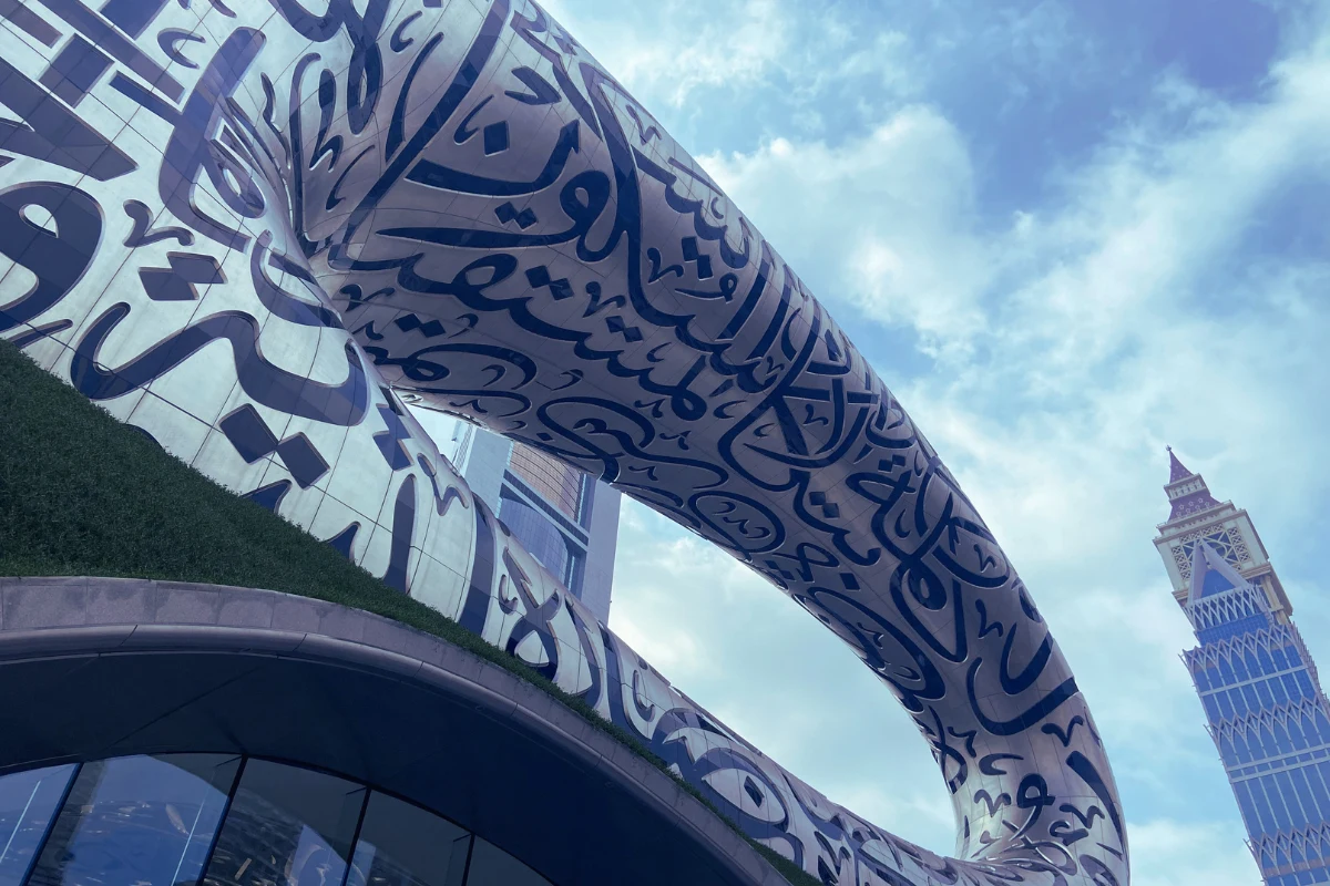 Low-angle shot of the iconic torus-shaped Museum of the Future in Dubai, featuring intricate Arabic calligraphy carved into the stainless steel facade against a clear blue sky.