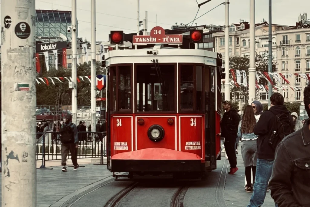 A vintage red and white tram passing down a narrow cobblestone street lined with historic European-style buildings in Istanbul.