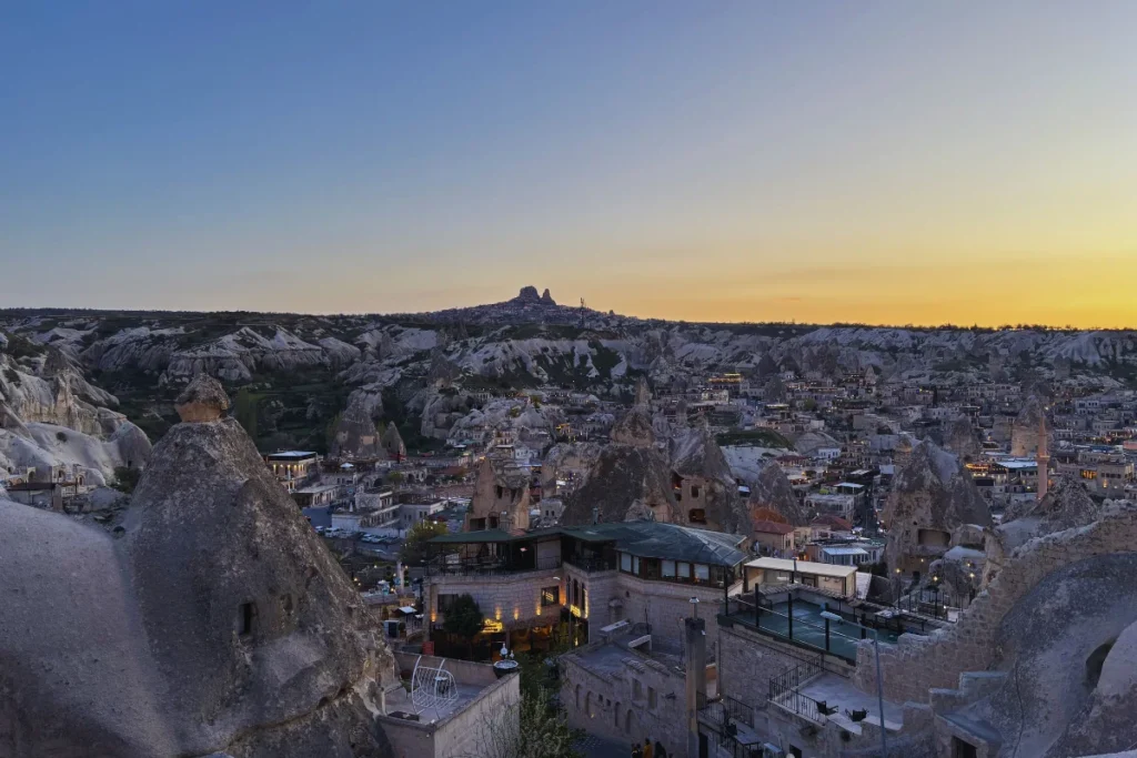 A wide evening shot looking out over a sharp cliff edge at a dense valley of white fairy chimneys as the sky fades.