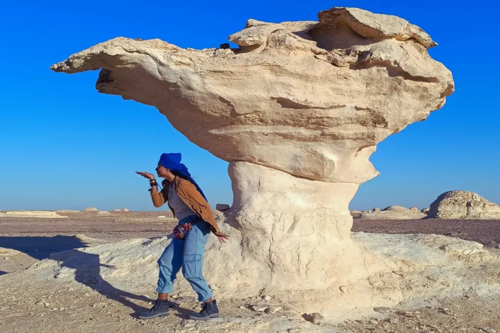 A striking, mushroom-shaped white chalk rock formation stands prominently against a clear blue sky in the White Desert.