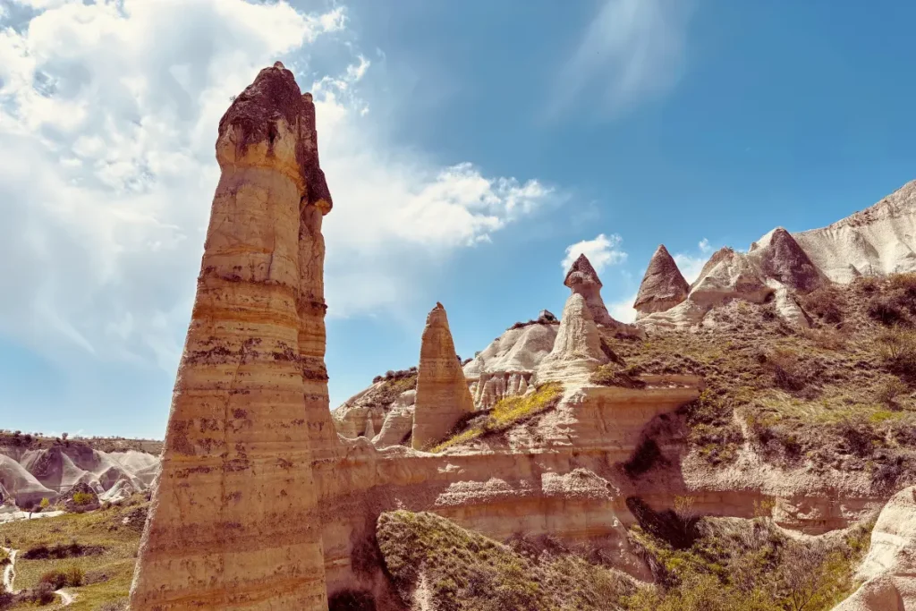 A close-up view of a very tall, slender, free-standing phallic stone pillar reaching towards a soft sky.