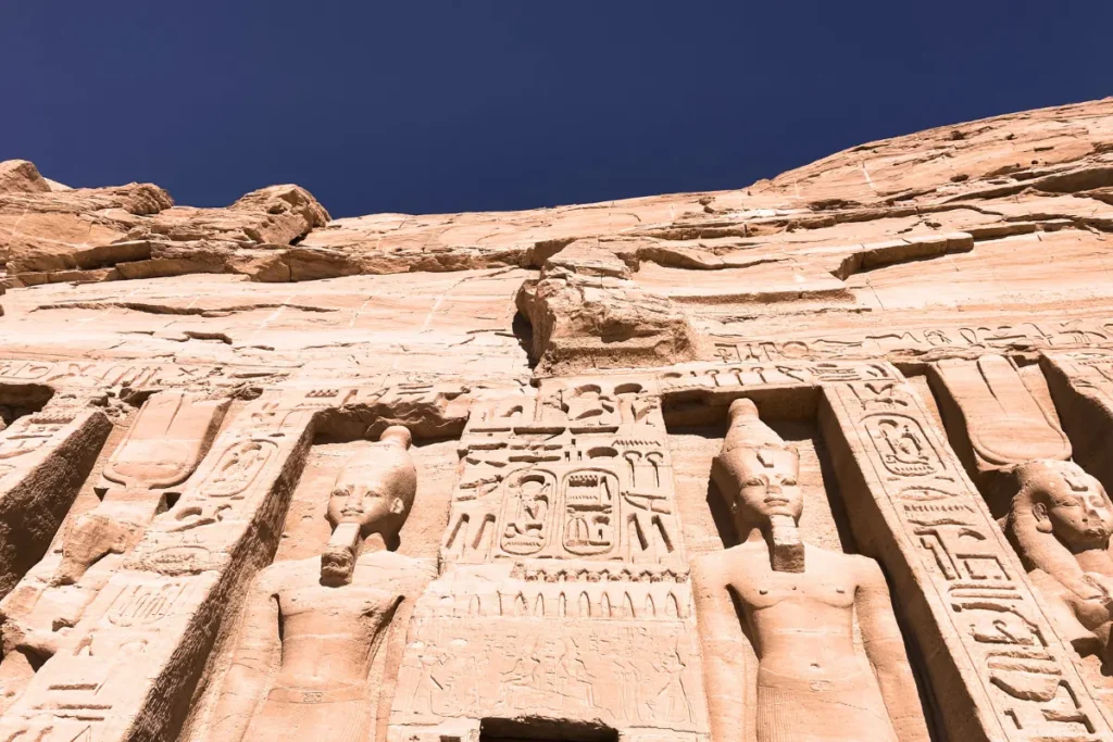 A outdoor shot of the massive stone facade of the Great Temple of Abu Simbel, featuring four colossal seated statues of Pharaoh Ramesses II.