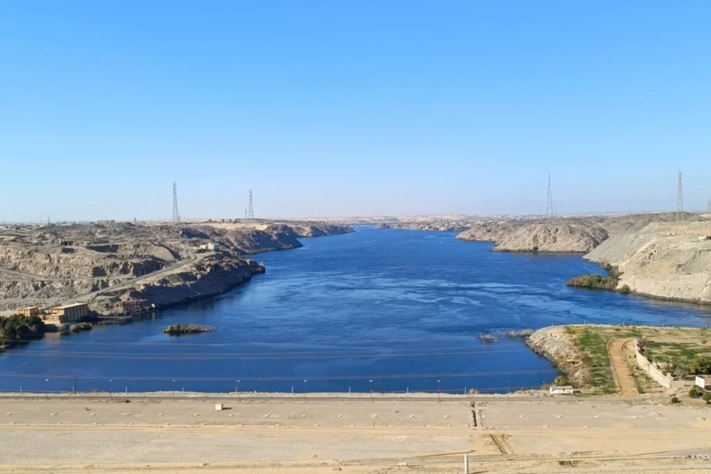 A high-angle view overlooking a deep blue reservoir bordered by rocky desert terrain at the Aswan High Dam.