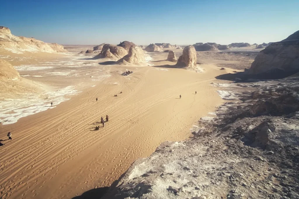 A high-angle panoramic view overlooking the deep, undulating sand canyons and white rock pillars of the Agabat Valley.