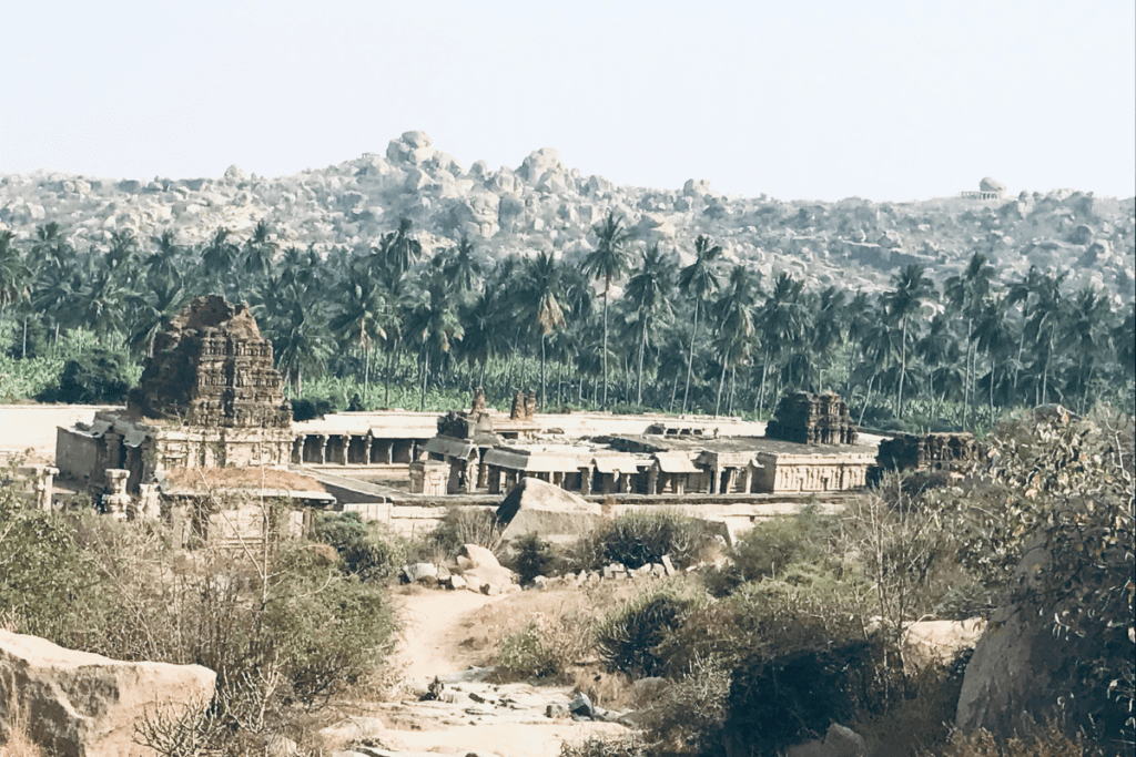 A wide-angle view of the large Achyutaraya Temple complex nestled between rocky hills and boulders.