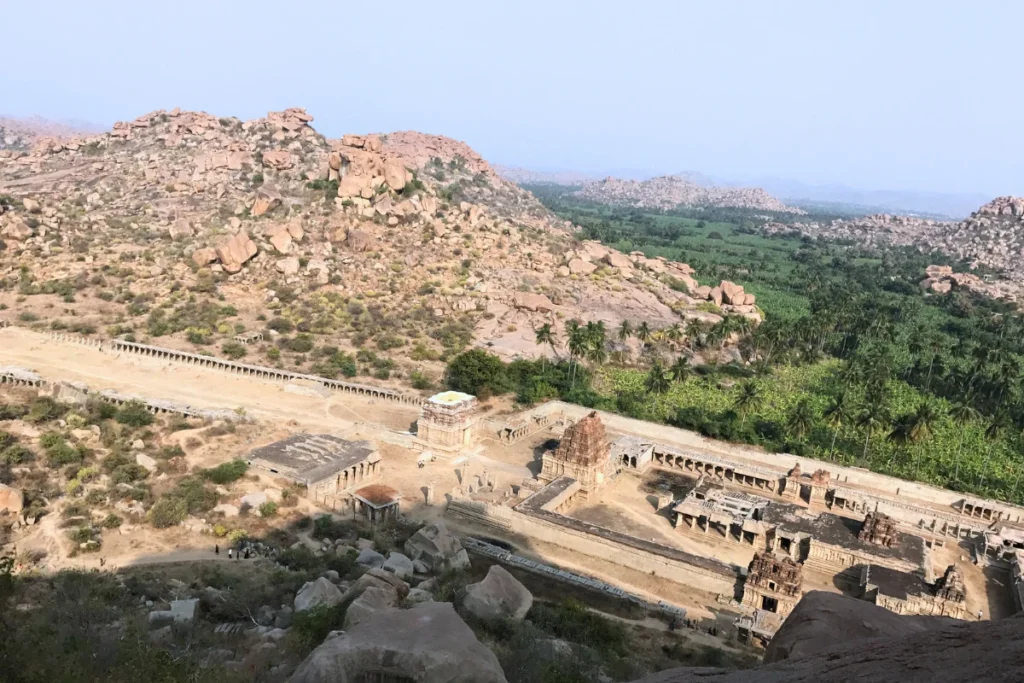  panoramic vista overlooking the green valleys, palm trees, and historic ruins scattered across Hampi as seen from Matanga Hill.