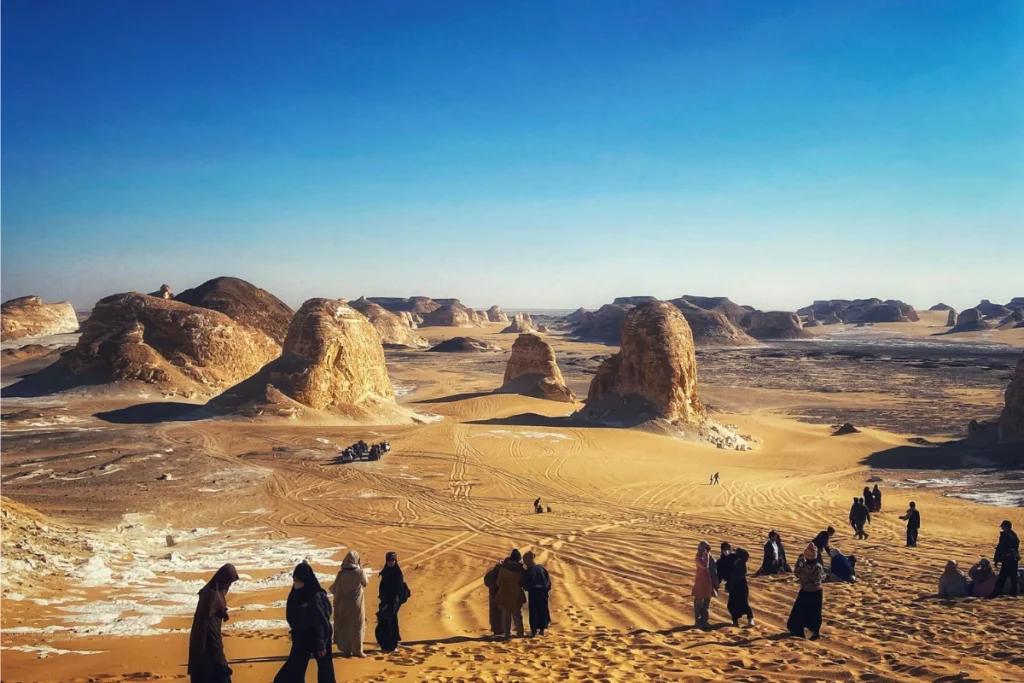 A view looking into a valley flanked by tall, pale yellow limestone cliffs and sand dunes.
