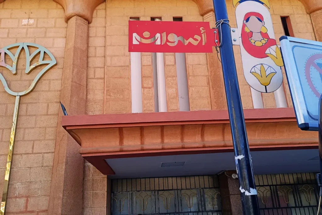 A shot of the Aswan station building's facade, decorated with a large stylized lotus flower graphic and signage in Arabic script.