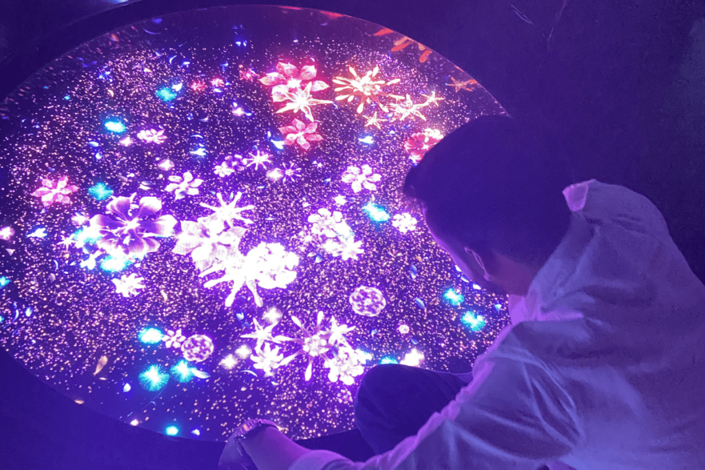 A vibrant room inside Aaya Universe filled with glowing neon blue and purple cosmic-themed light displays reflecting onto a glossy floor.