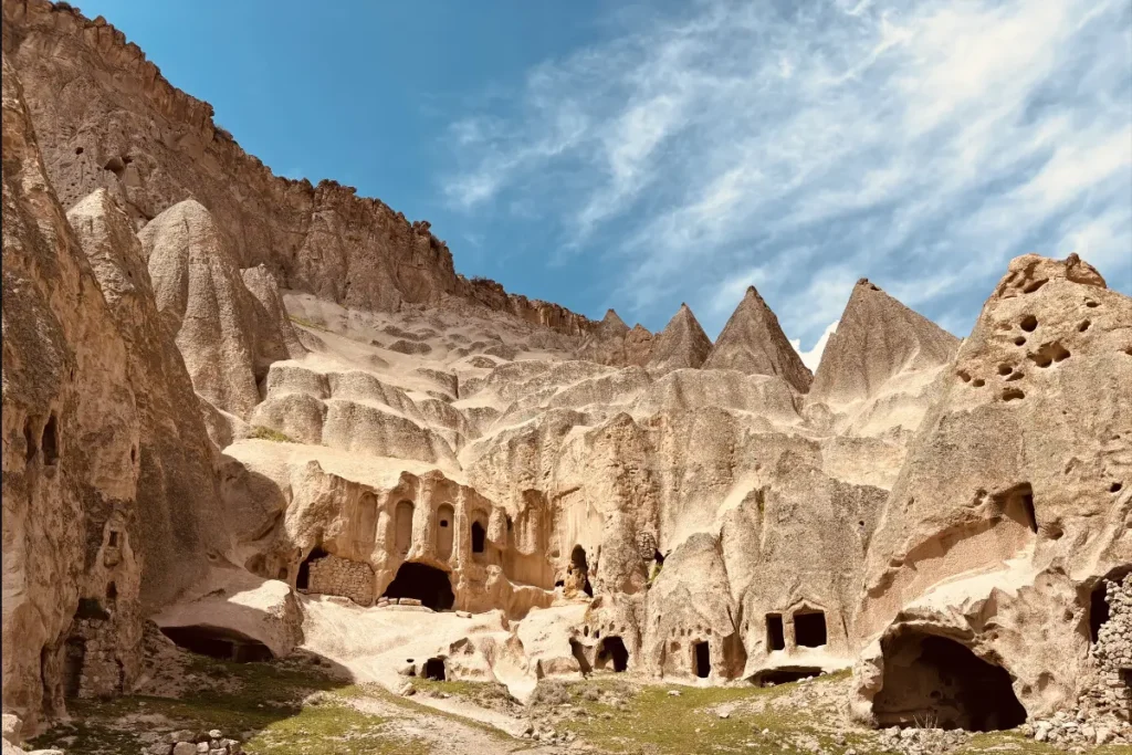A high-angle shot of a massive, multi-level rock citadel with deep, carved columned facades built straight into a steep hill.