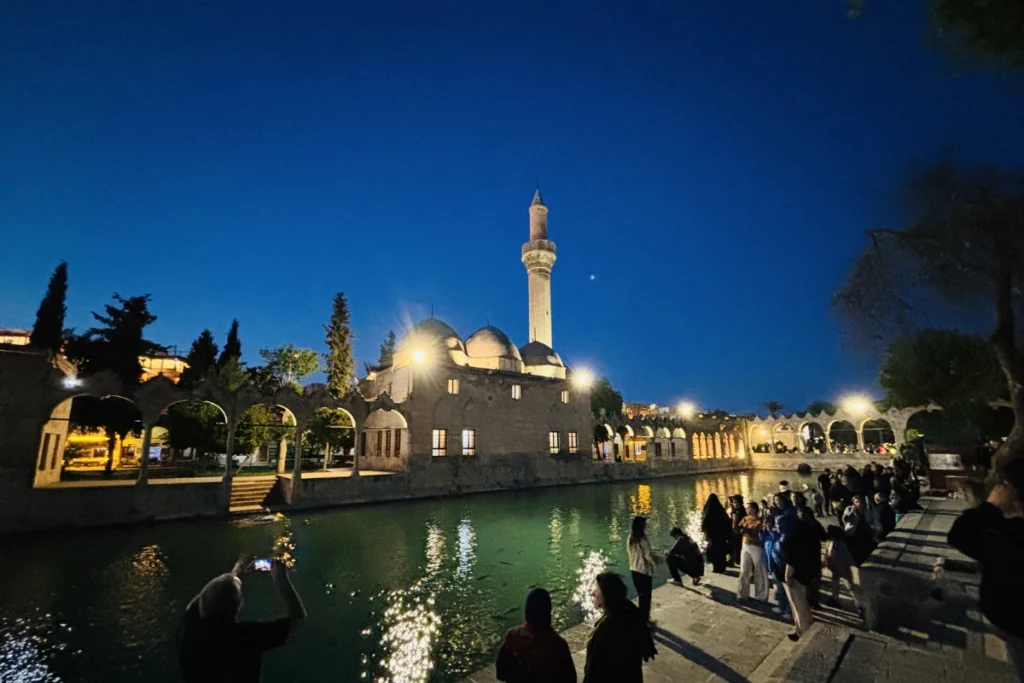 The peaceful Balıklıgöl sacred pool complex at dusk, reflecting illuminated stone arches, minarets, and surrounding mosque architecture.