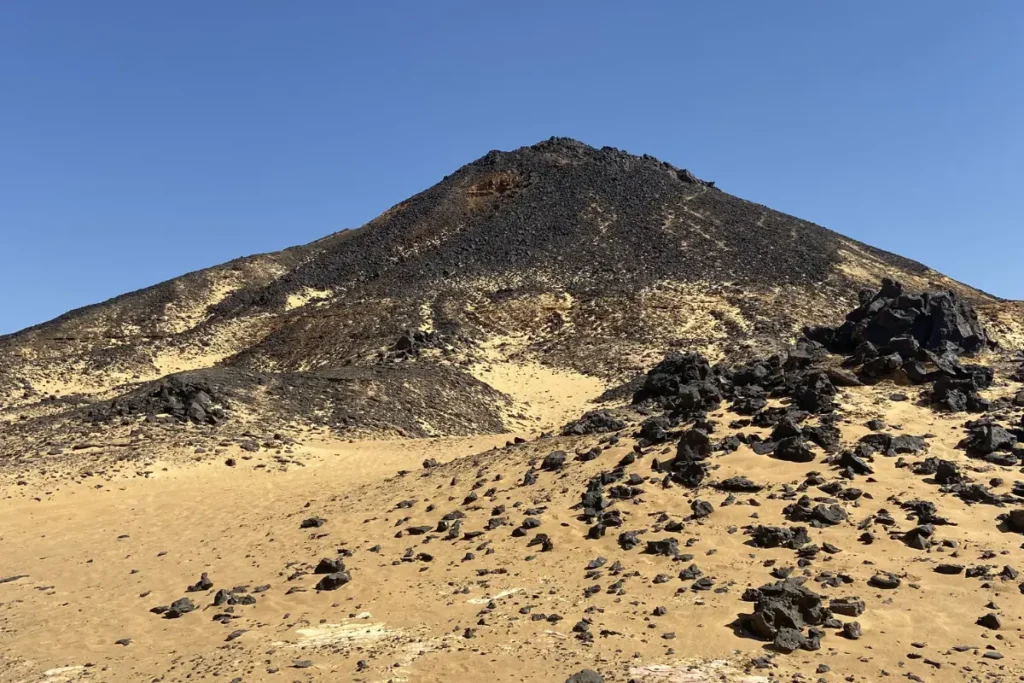 A steep, cone-shaped hill covered in dark basalt stone and volcanic debris.