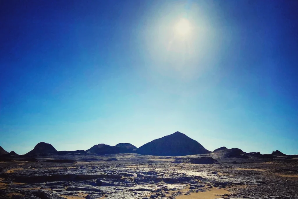 A panoramic view from atop a hill showing black-dusted volcanic mounds stretching across the sandy desert floor.