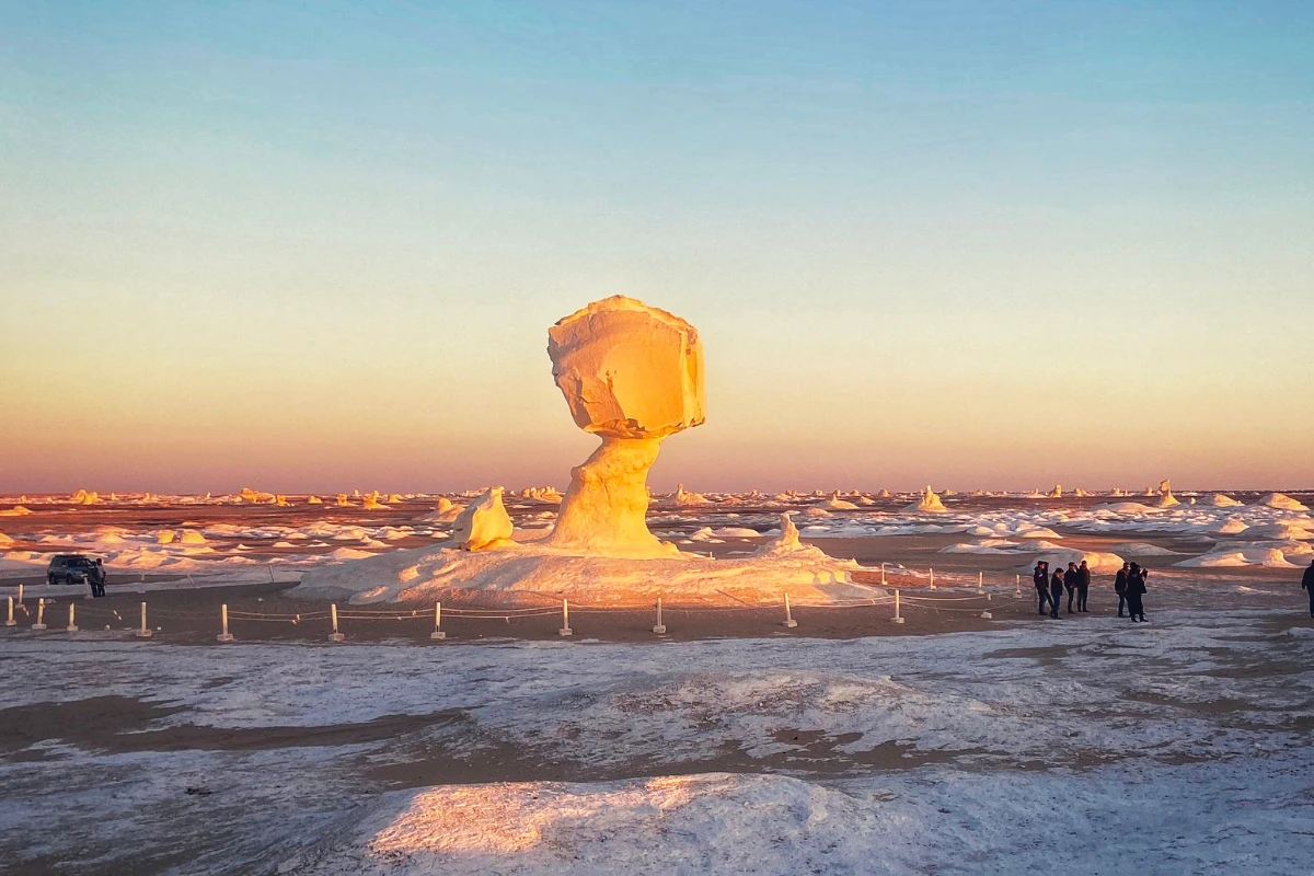 A wide landscape of the Egyptian White Desert featuring a large mushroom-shaped limestone rock formation surrounded by snowy-looking chalk