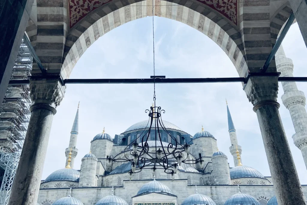 The magnificent multi-domed Blue Mosque in Istanbul, framed by green trees under a clear blue sky.