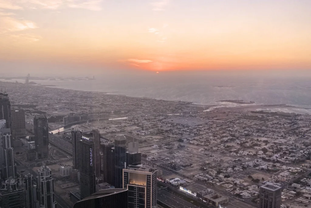 A dramatic sunset view looking out from a high-altitude observation deck across the sprawling urban grid of Dubai.