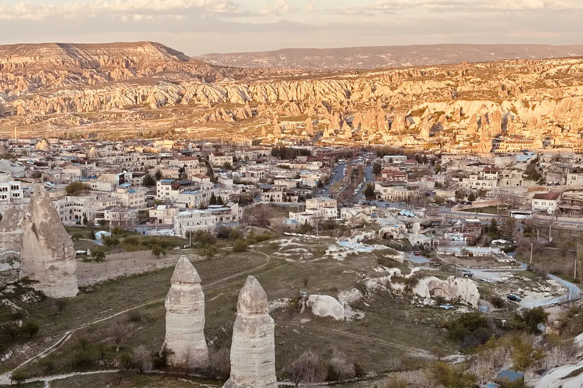An aerial perspective of Göreme displaying white stone buildings, cave dwellings, and tall fairy chimney rock structures under warm sunlight.