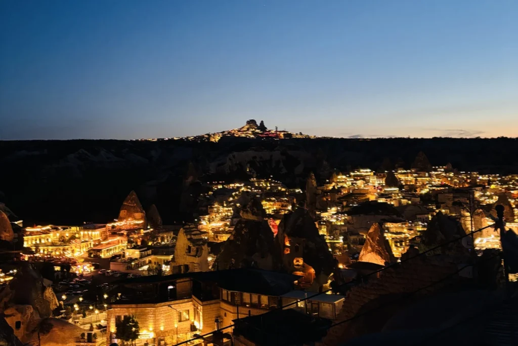 A beautiful twilight panorama of an ancient town lit by golden streetlights nestled amidst sharp, dark rock hills.