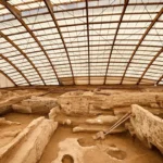 Wide view of the archaeological excavation site of Çatalhöyük covered by a large protective modern roof structure.