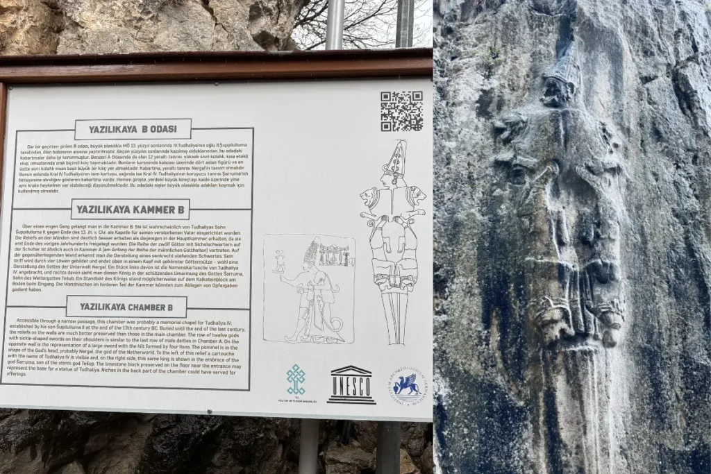  A white informational sign providing text and illustrations about Chamber B and the Sword God. A tall, vertical rock carving depicting the detailed figure of the Hittite underworld deity, the Sword God Nergal.