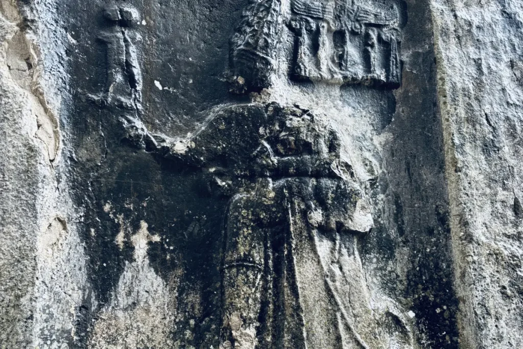 A detailed stone relief carved directly into a rock face, depicting a large divine figure in profile holding a smaller figure.