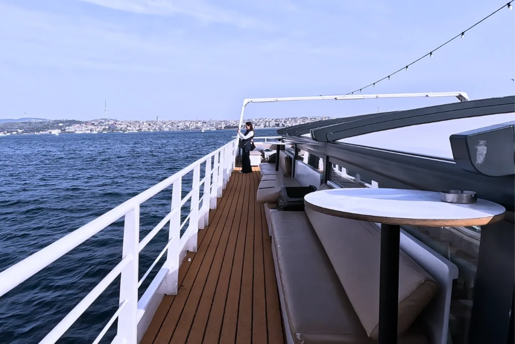 View from the wooden deck of a cruise ship looking out over the blue waters of the Bosphorus Strait.
