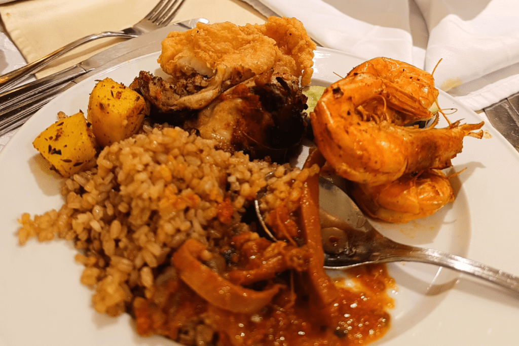 A platter featuring rice, grilled shrimp, fish, calamari, and roasted quail served on a dining table.