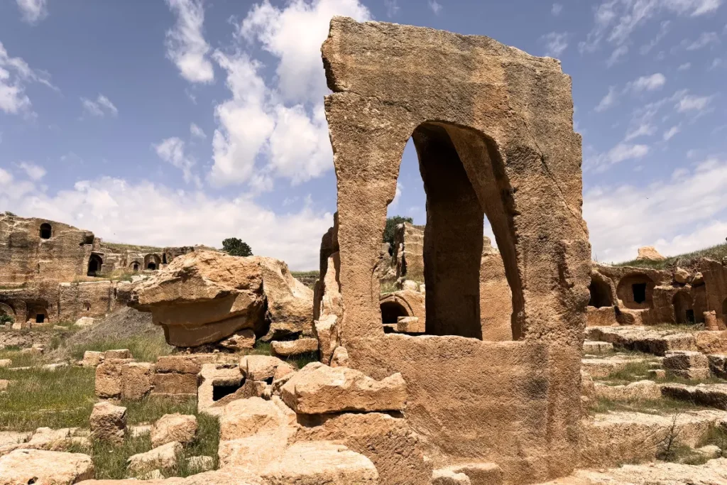 A tall, ancient stone archway standing amid ruins under a bright blue sky at the Dara archaeological site.