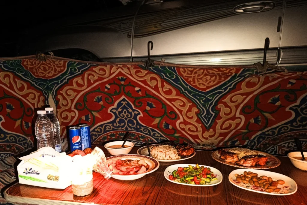 A spread of traditional Egyptian dishes, including bread, dips, and salads, laid out on a low table inside a patterned fabric tent.