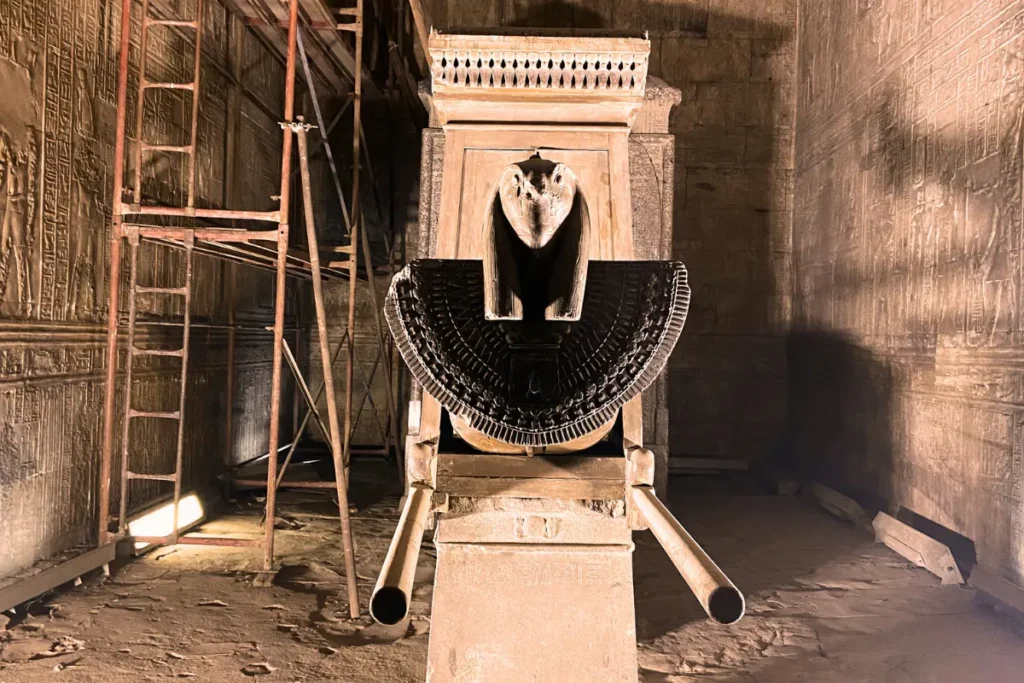 A dark, dramatic shot of a black stone statue of the falcon god Horus wearing the double crown of Egypt inside the Temple of Edfu.