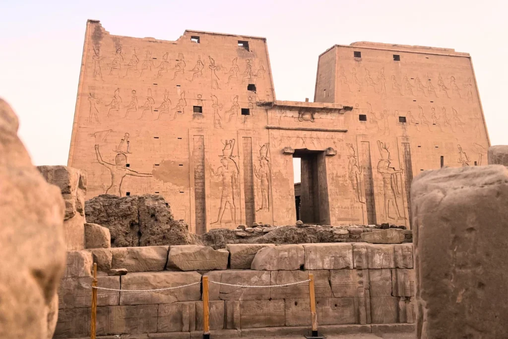 A view of the massive, well-preserved stone entrance pylon of the Temple of Edfu under a clear sky.