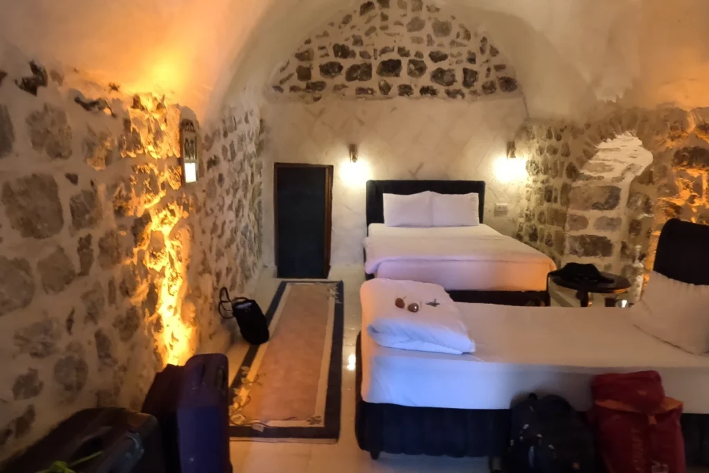 An interior shot of a unique hotel room built inside a stone cave, featuring two neatly made twin beds.