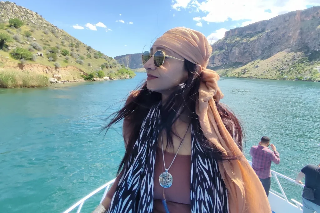 Sumana standing on a boat deck, posing against the scenic rocky cliffs of the Euphrates River.
