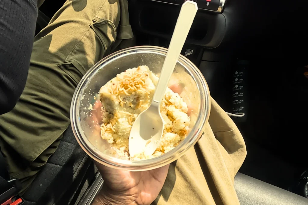 A first-person view of someone holding a plastic cup filled with a street food snack and a spoon.