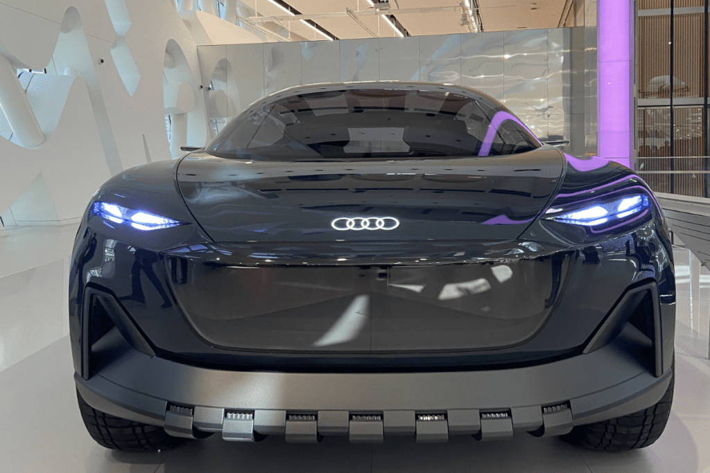 A sleek, futuristic black concept car with glowing blue headlights and minimalist design features displayed inside an exhibition room.