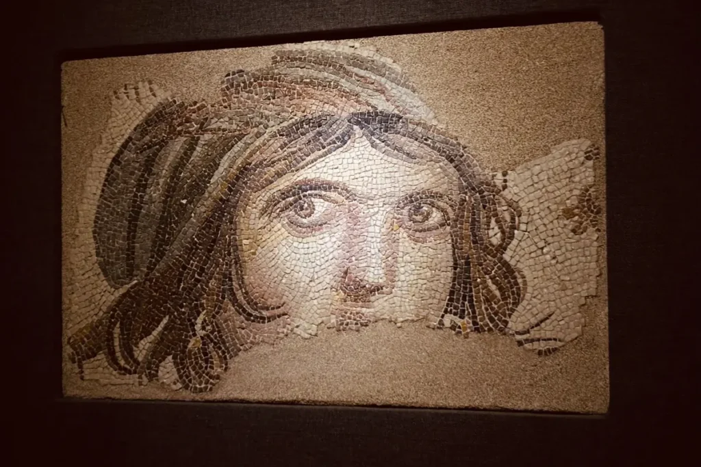A close-up of the famous "Gypsy Girl Mosaic" at the Zeugma Mosaic Museum, featuring a face with striking, expressive dark eyes.