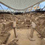 Ancient stone structures and circular compounds of Göbekli Tepe under an open-air protective shelter.