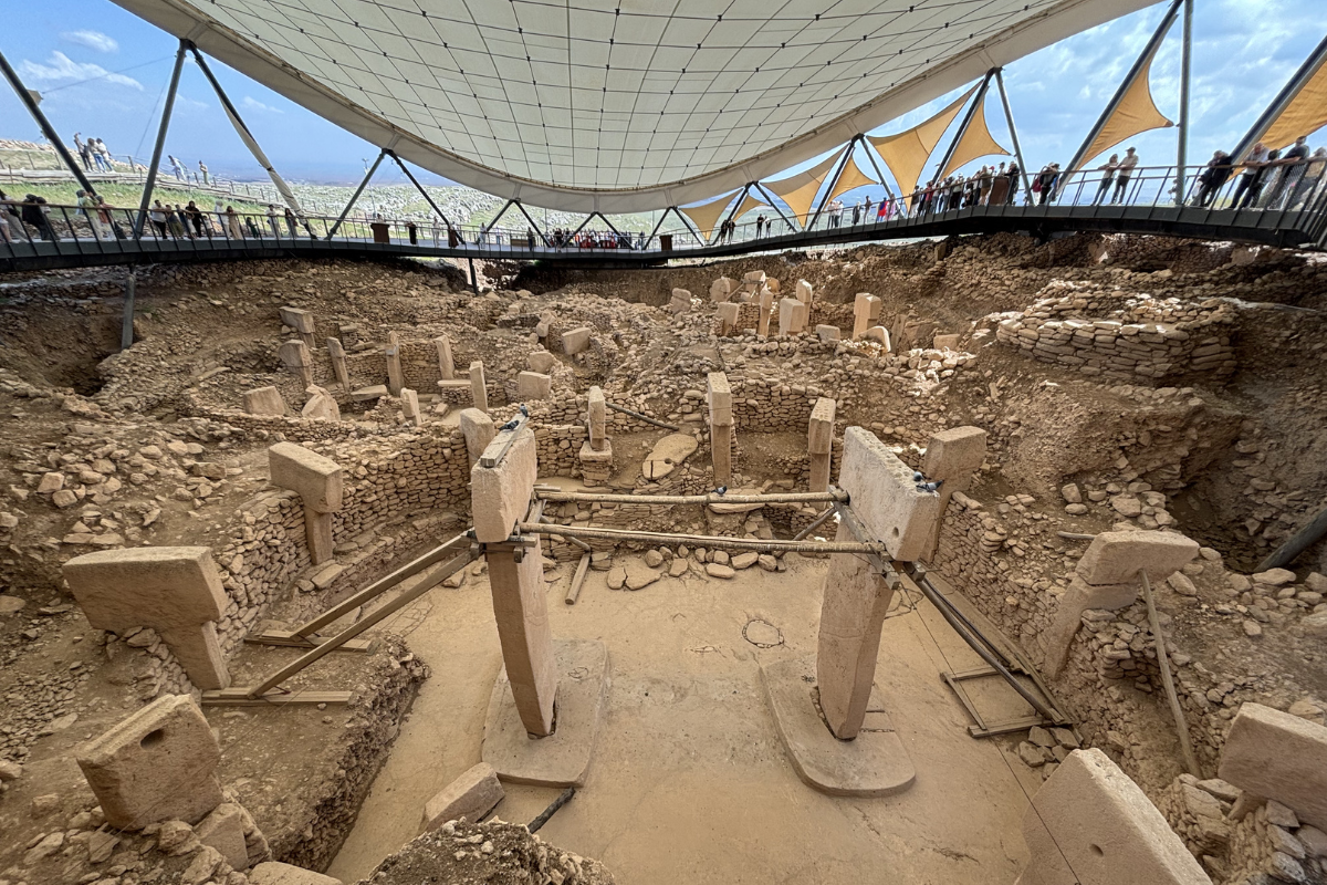 Ancient stone structures and circular compounds of Göbekli Tepe under an open-air protective shelter.