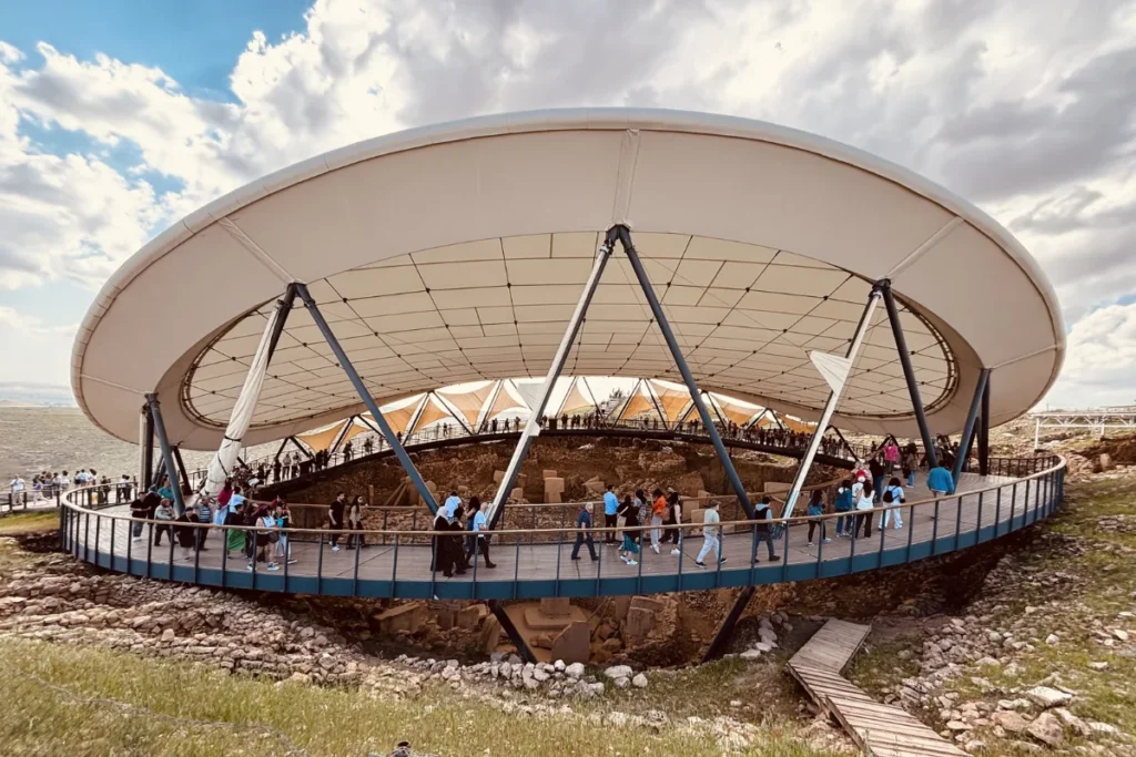 A wide-angle view of the large circular stone enclosures and towering T-shaped pillars of Göbekli Tepe under its permanent architectural shelter.