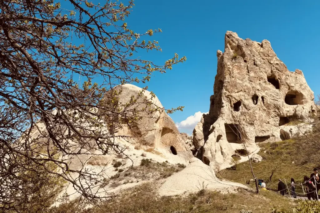 A steep, towering cone-shaped rock structure with small carved windows reaching into a clear blue sky.