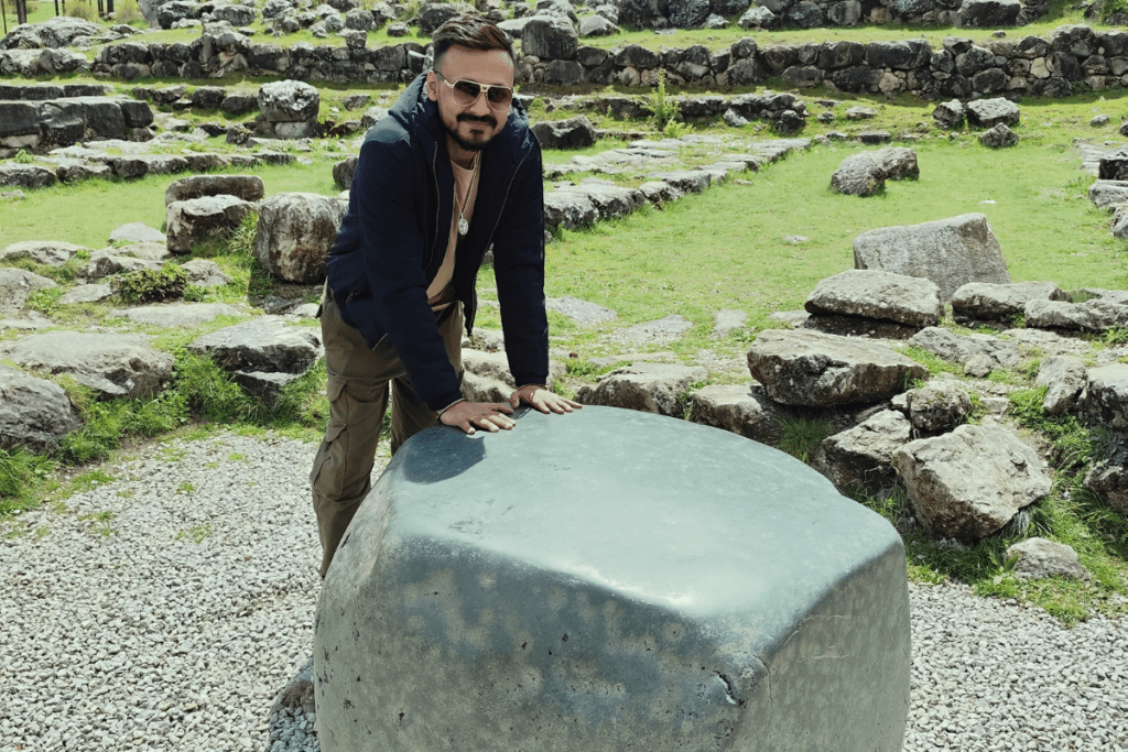 Akash leaning forward to place his hands on the large green wish stone surrounded by ruins.