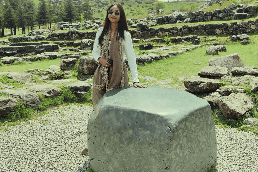 Sumana standing next to a large, rectangular block of polished green nephrite stone among ancient foundations.