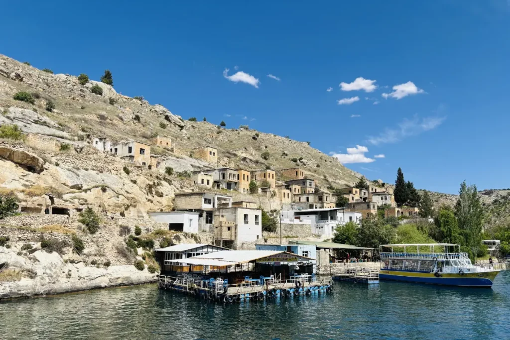 A scenic view of old stone houses terraced along a rugged desert hillside overlooking the Euphrates River in Halfeti.