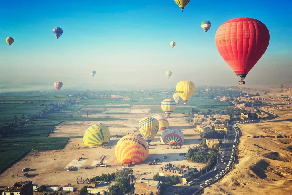 Colorful hot air balloons floating over the landscape during a bright orange sunrise.