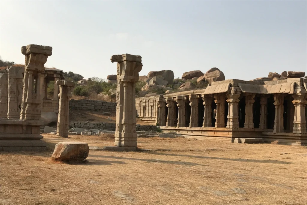 Hampi Ruins A row of ancient carved granite pillars and stone pavilion halls standing on a dusty plain backed by rocky hills.