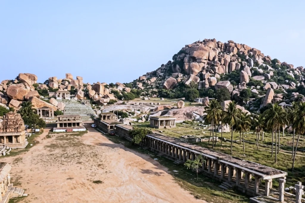 A distant shot showing the long, historic columned structures of Hampi Bazaar situated at the base of the rocky Matanga Hill.