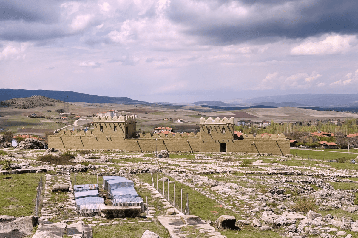 A wide view of a reconstructed section of the stone and mud-brick fortifications at Hattusa, under a bright blue sky.