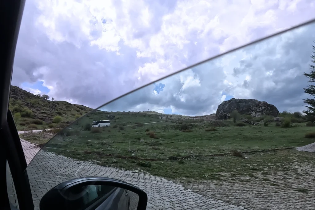 A scenic landscape view of green fields and rolling hills seen through a car window while driving on a rural road.