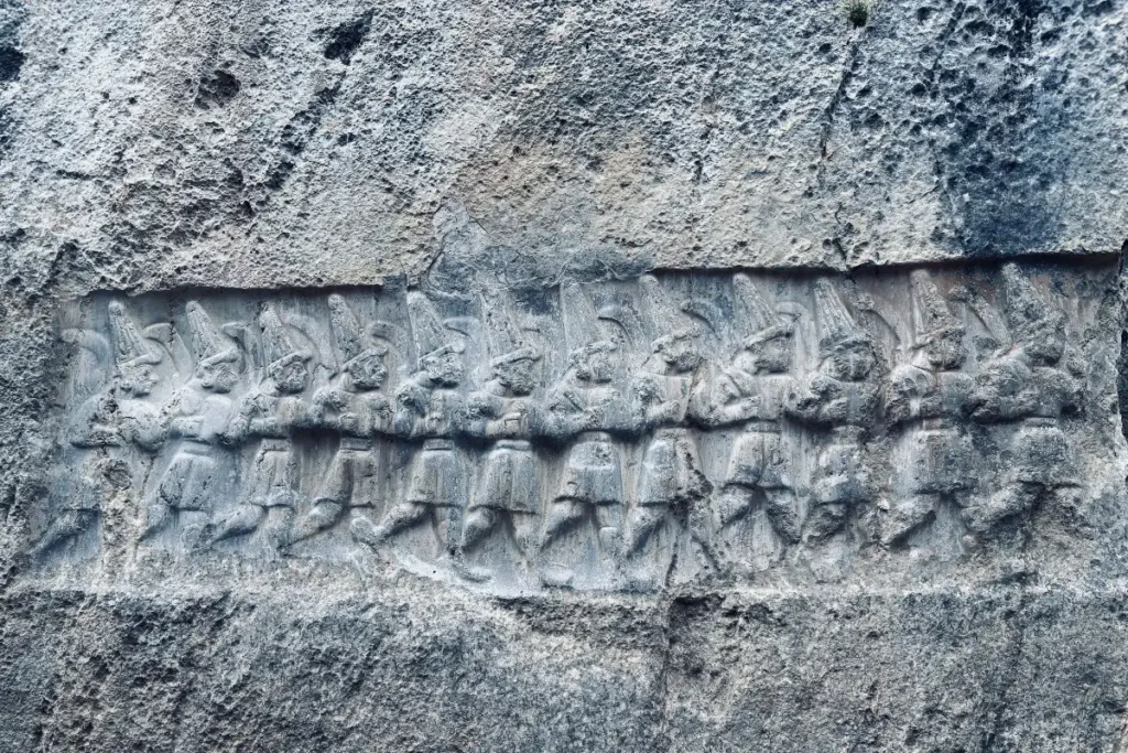 A detailed view of a rough stone slab covered in ancient GOD CARVINGS AT YAZILIKIYA.