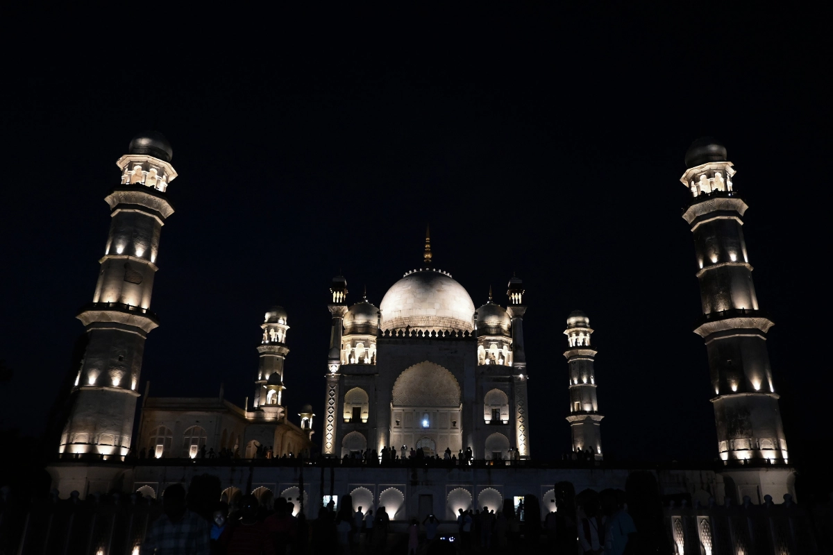 A symmetrical night view of the illuminated Bibi Ka Maqbara in Chhatrapati Sambhajinagar, Maharashtra, showcasing its central marble dome and flanking minarets glowing under dark skies.